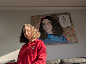 Yael sitting in front of her self-portrait 20/25 Vision hanging on the wall